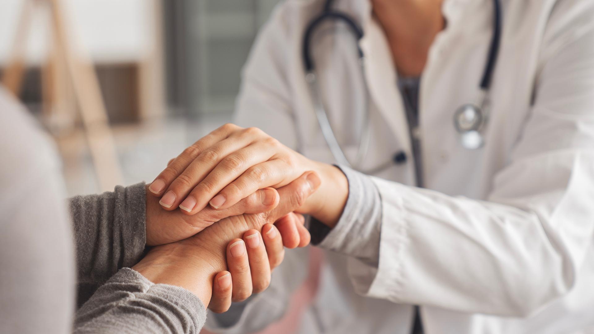 A doctor in a white coat holds a patient's hands.