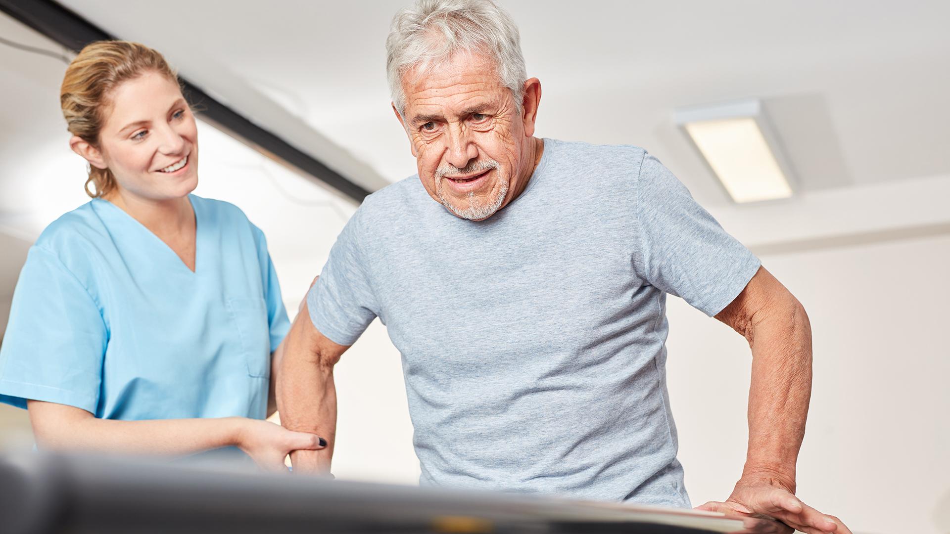 A physical therapist assists a man using bars for support in walking.