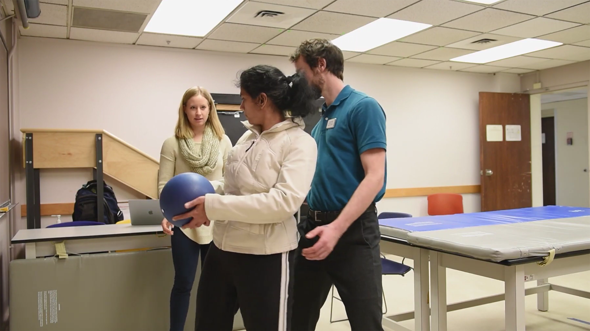 A man assists a woman using a ball to perform a twisting exercise.