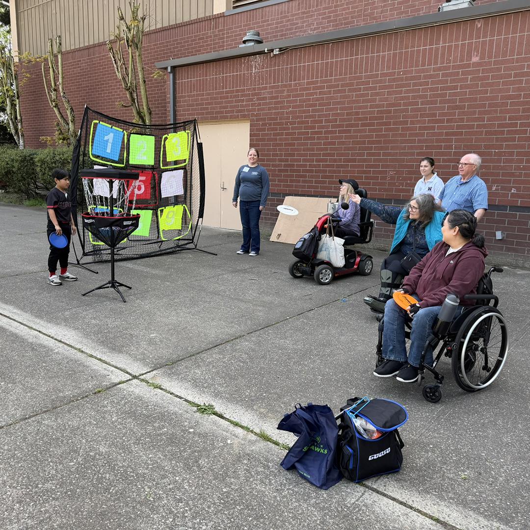 A group of people, some in wheelchairs, practice tossing a ball at a target.