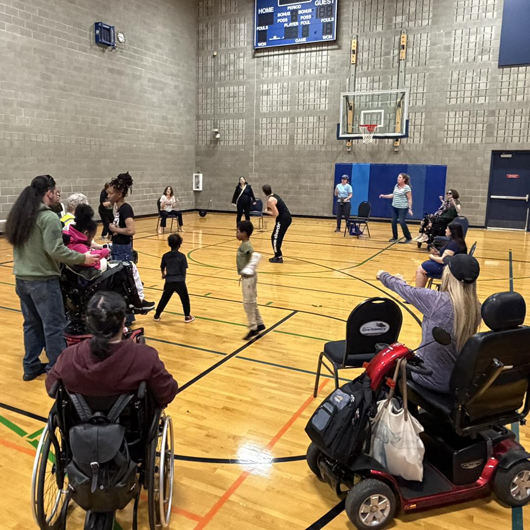 A group of people, some in wheelchairs, play a game in a gym.