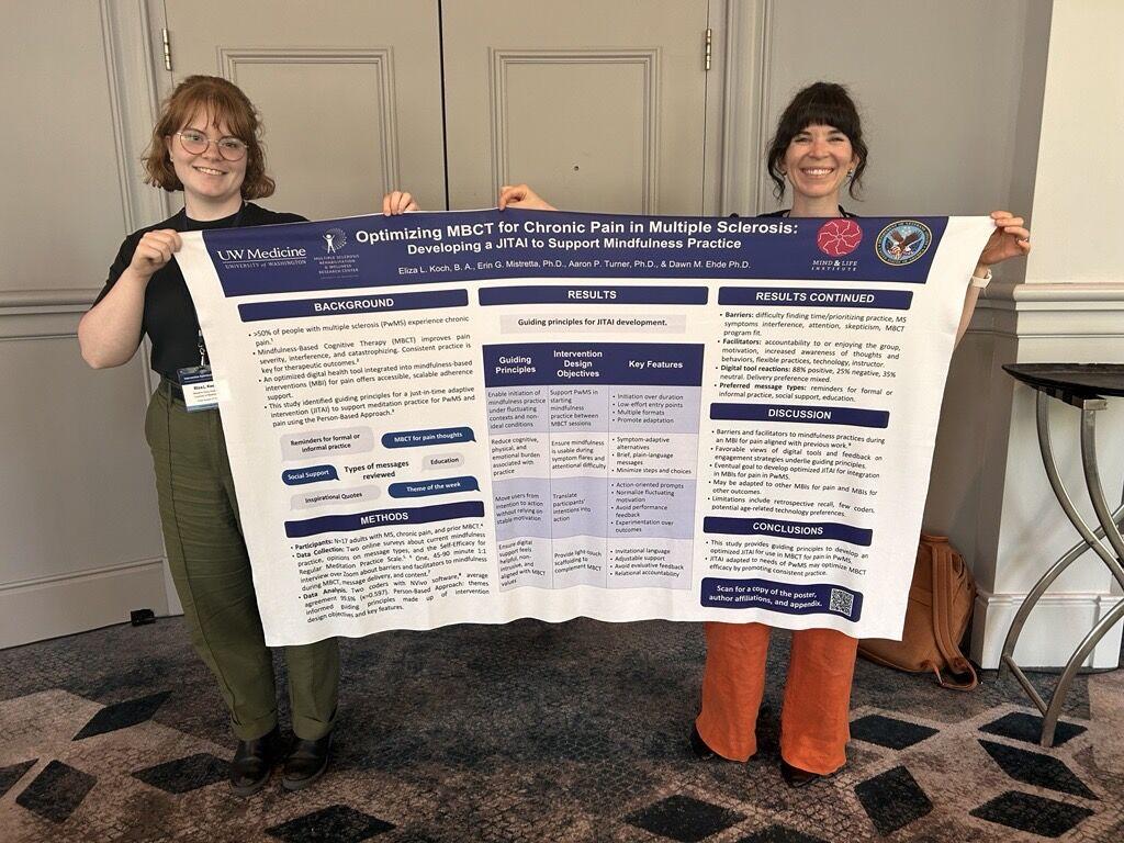 Two women hold up an academic poster.