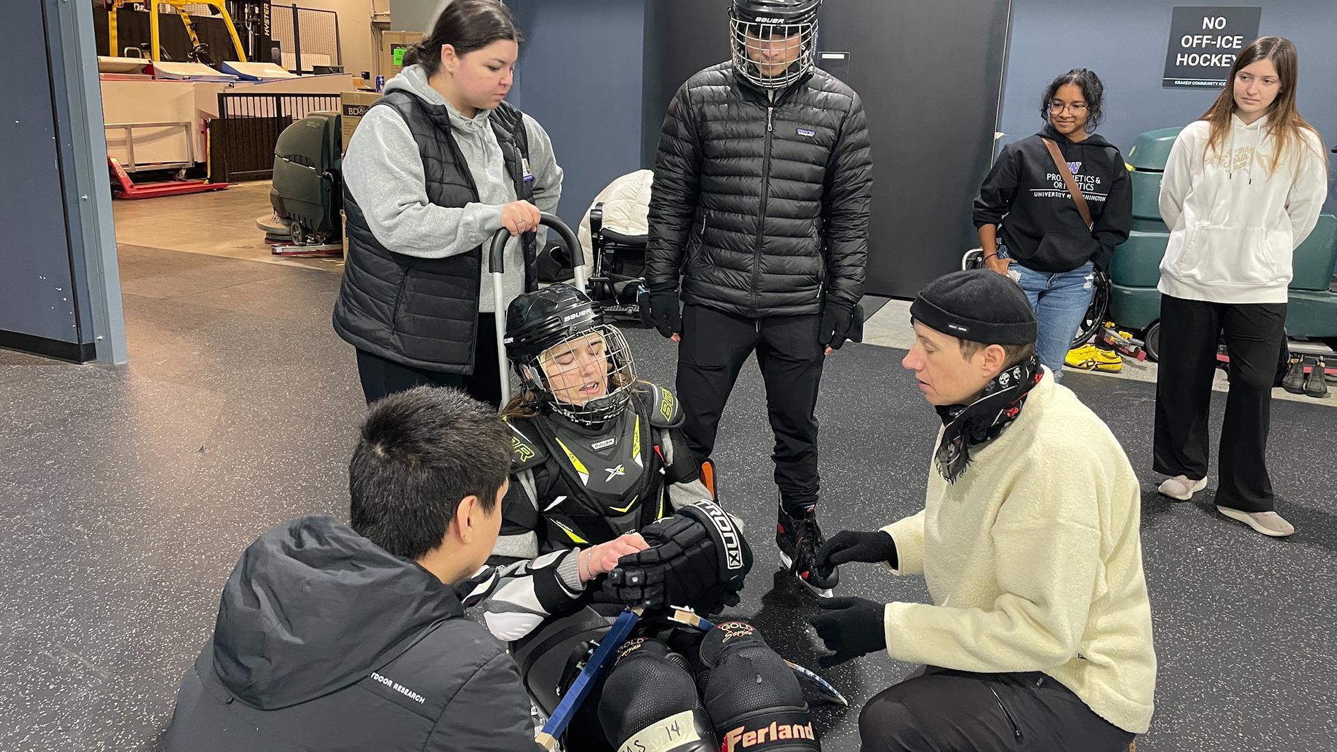 Volunteers help a sled hockey athlete gear up for practice.