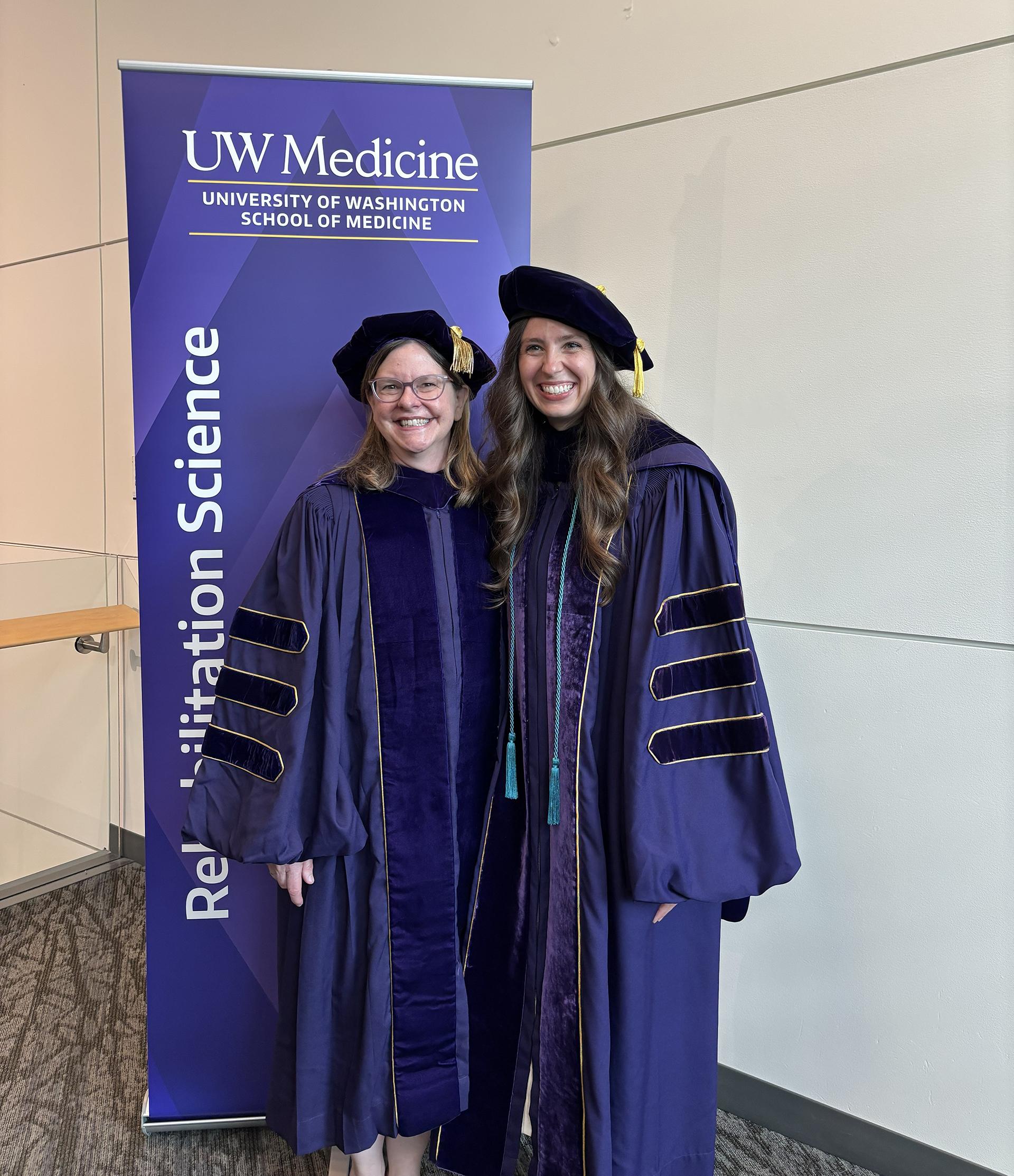 Two women in PhD regalia smile at the camera.