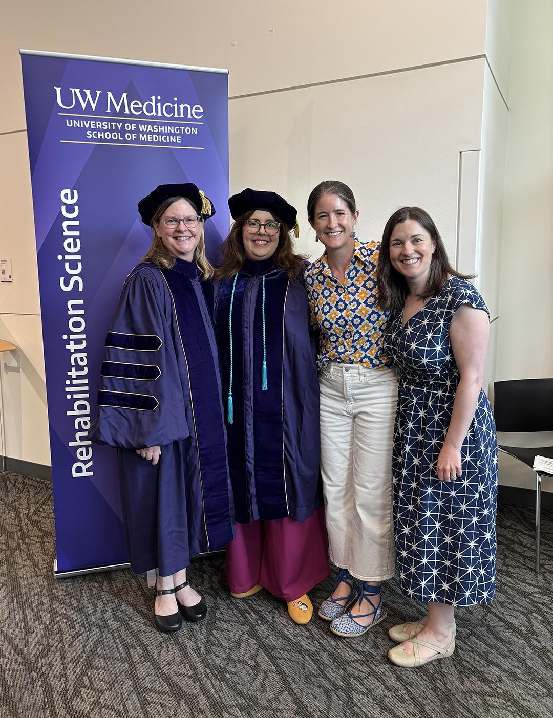 Four women, two in PhD regalia, smile at the camera.