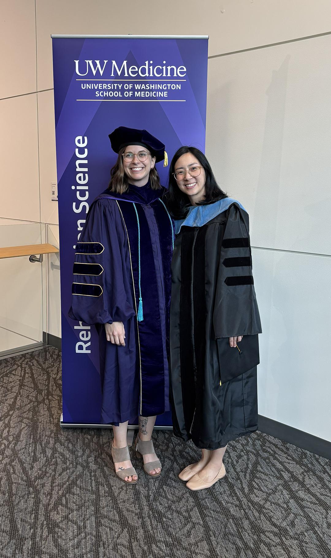 Two women in PhD regalia smile at the camera.