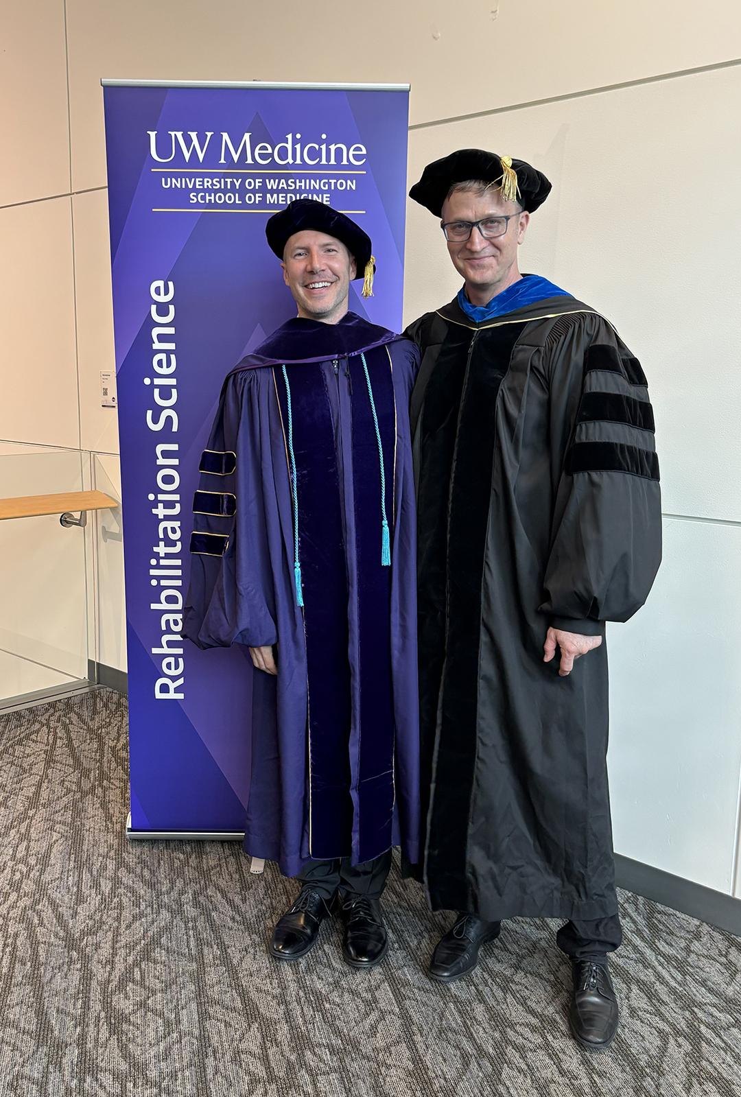 Two men in PhD regalia smile at the camera.