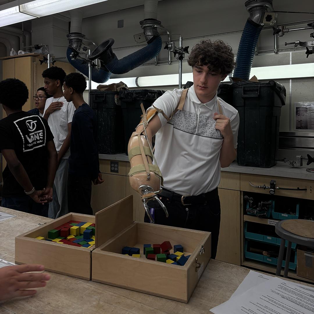 A student tries to pick up blocks with a prosthetic arm.