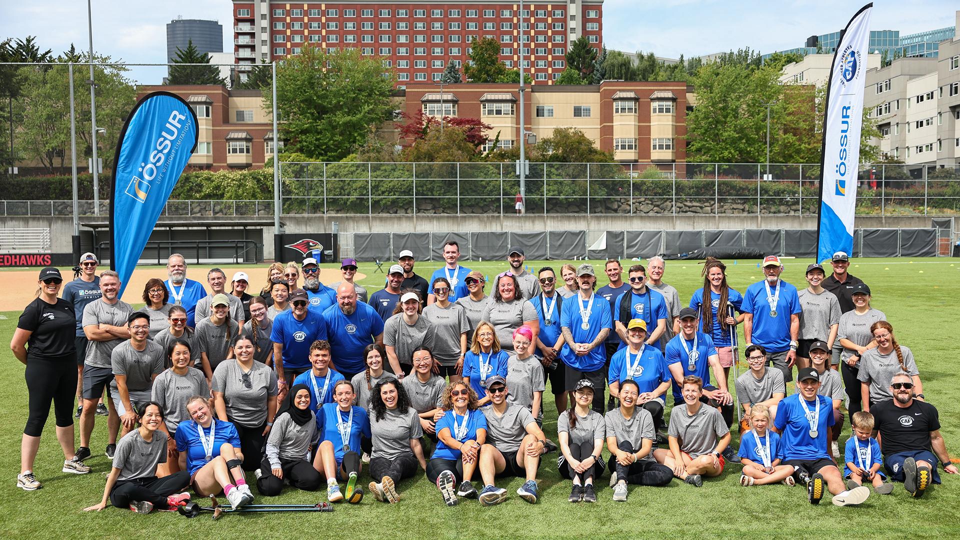 A large group of people in grey and blue t-shirts pose in a playing field.