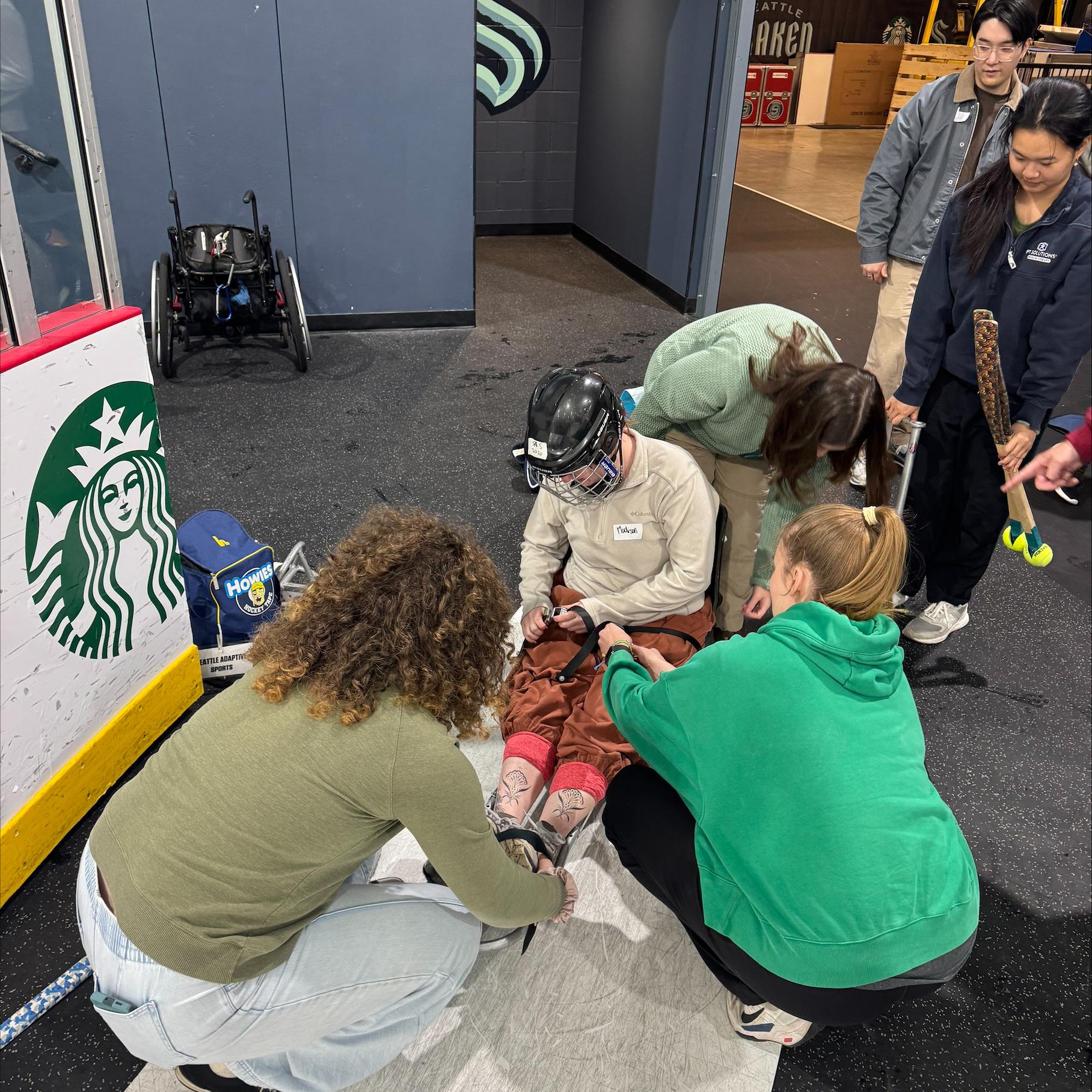 A sled hockey athlete gets help putting on gear.