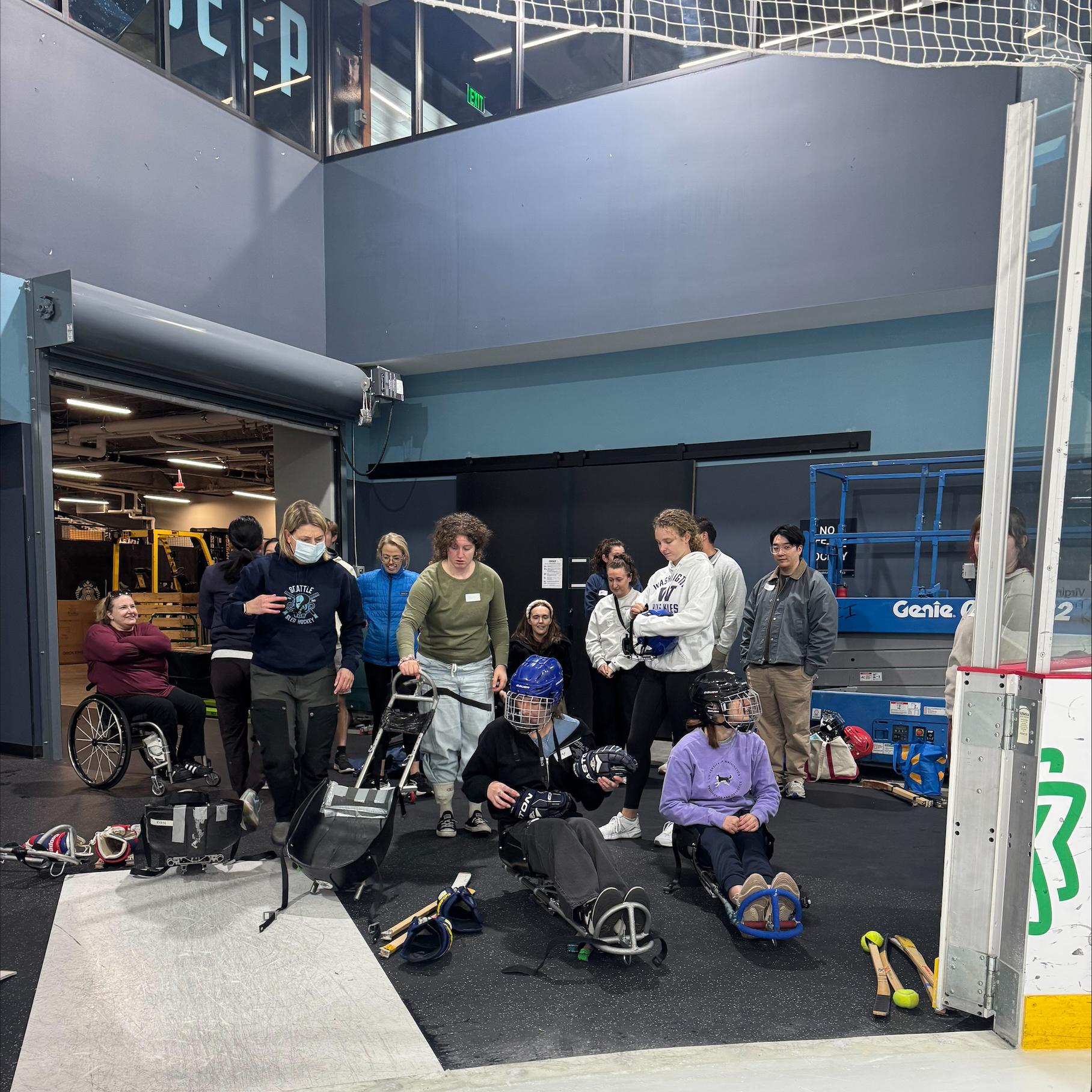 A group of people getting ready to play sled hockey in an arena.