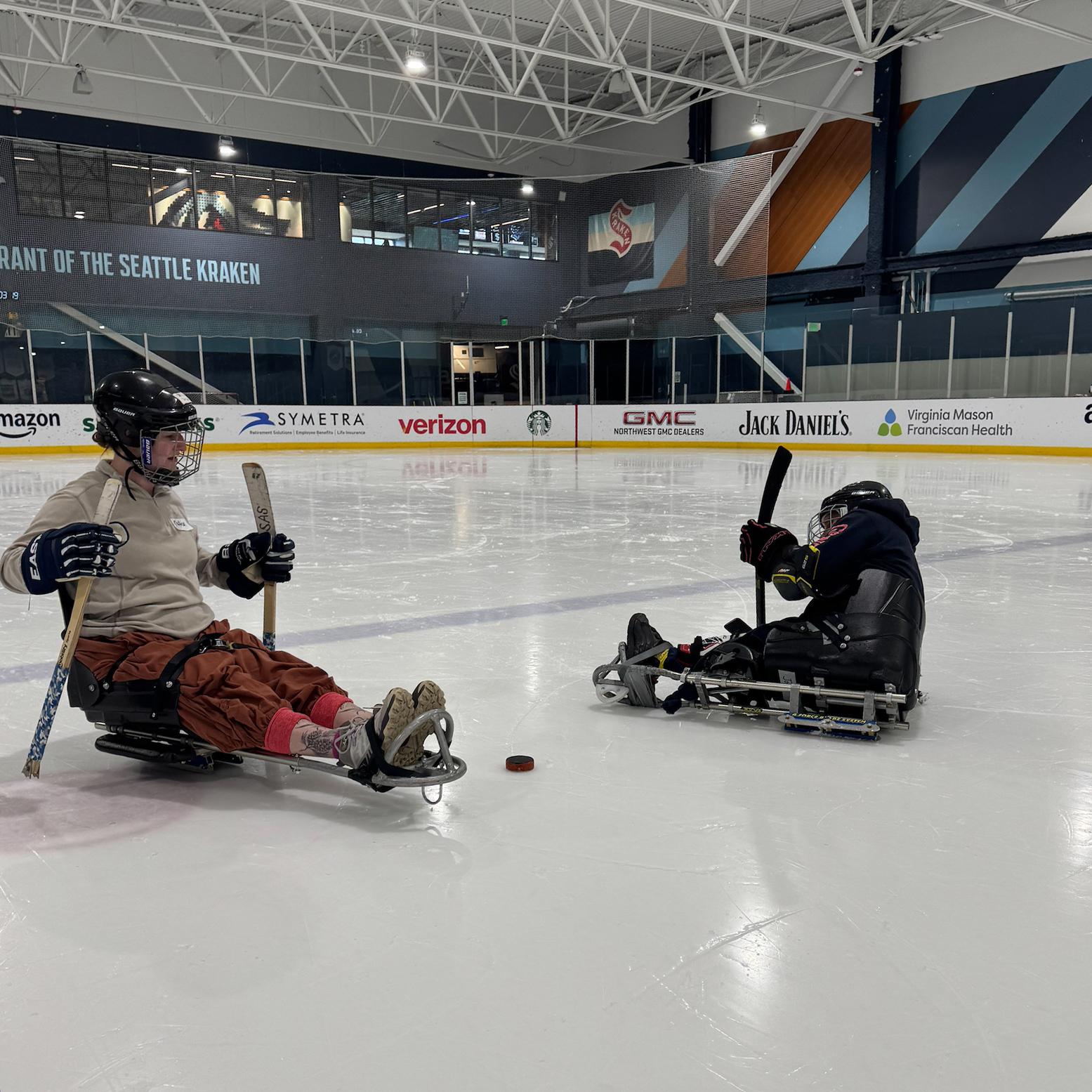 Two sled hockey players chase the puck.